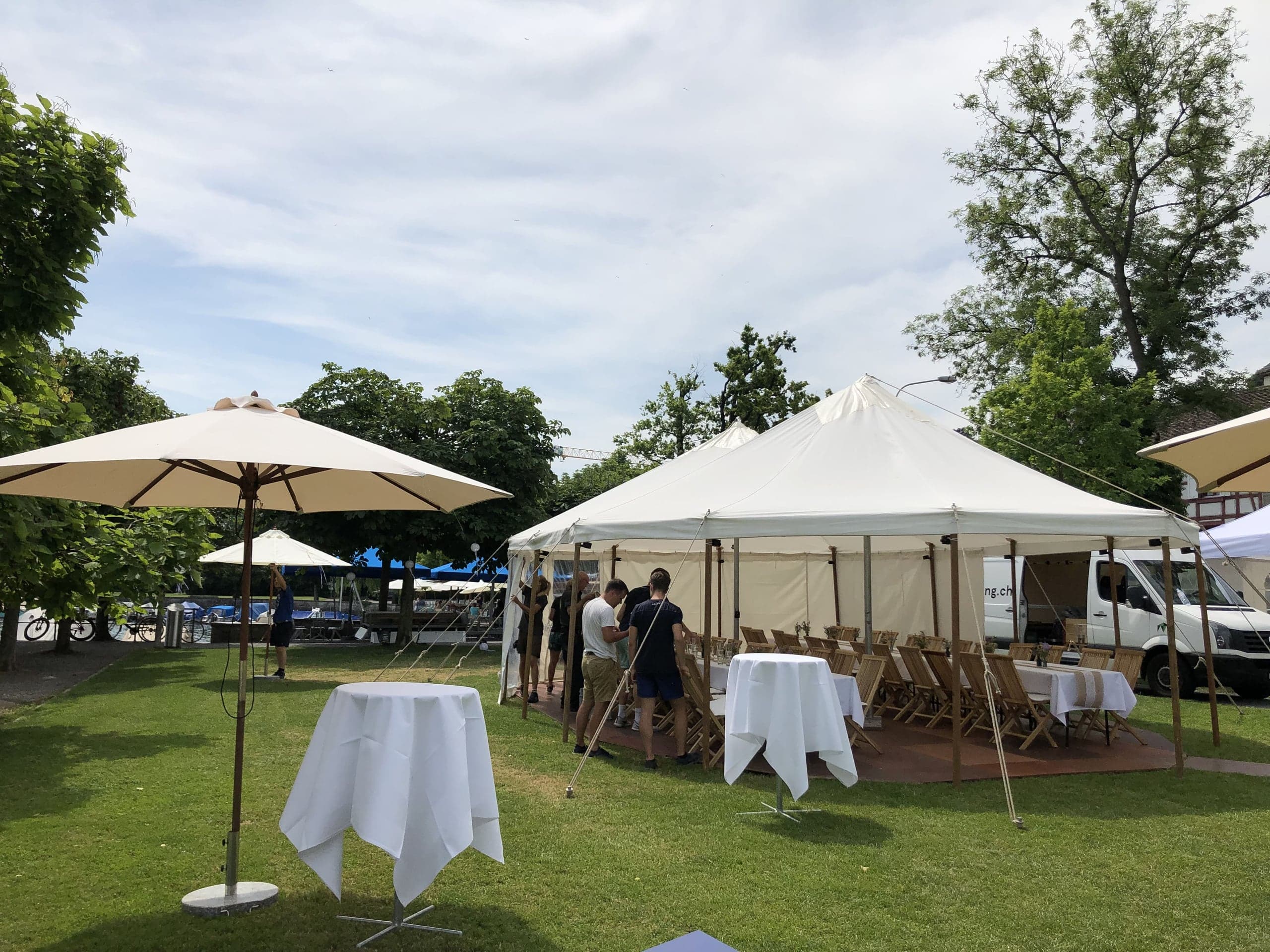 Apéro mit Stehtischen und Sonnenschirmen neben einem Stoffzelt